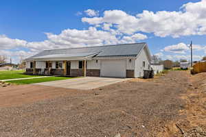 View of front of property with driveway, board and batten siding, covered porch, an attached garage, and a metal roof
