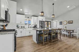 Kitchen with stainless steel appliances, light stone countertops, white cabinetry, a center island, and a kitchen bar