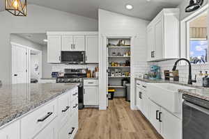 Kitchen featuring lofted ceiling, light stone counters, white cabinets, black appliances, and light wood finished floors