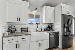 Kitchen with stainless steel fridge with ice dispenser, white cabinets, and dark stone counters