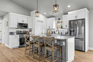 Kitchen with stainless steel appliances, light stone counters, white cabinetry, vaulted ceiling, and decorative light fixtures
