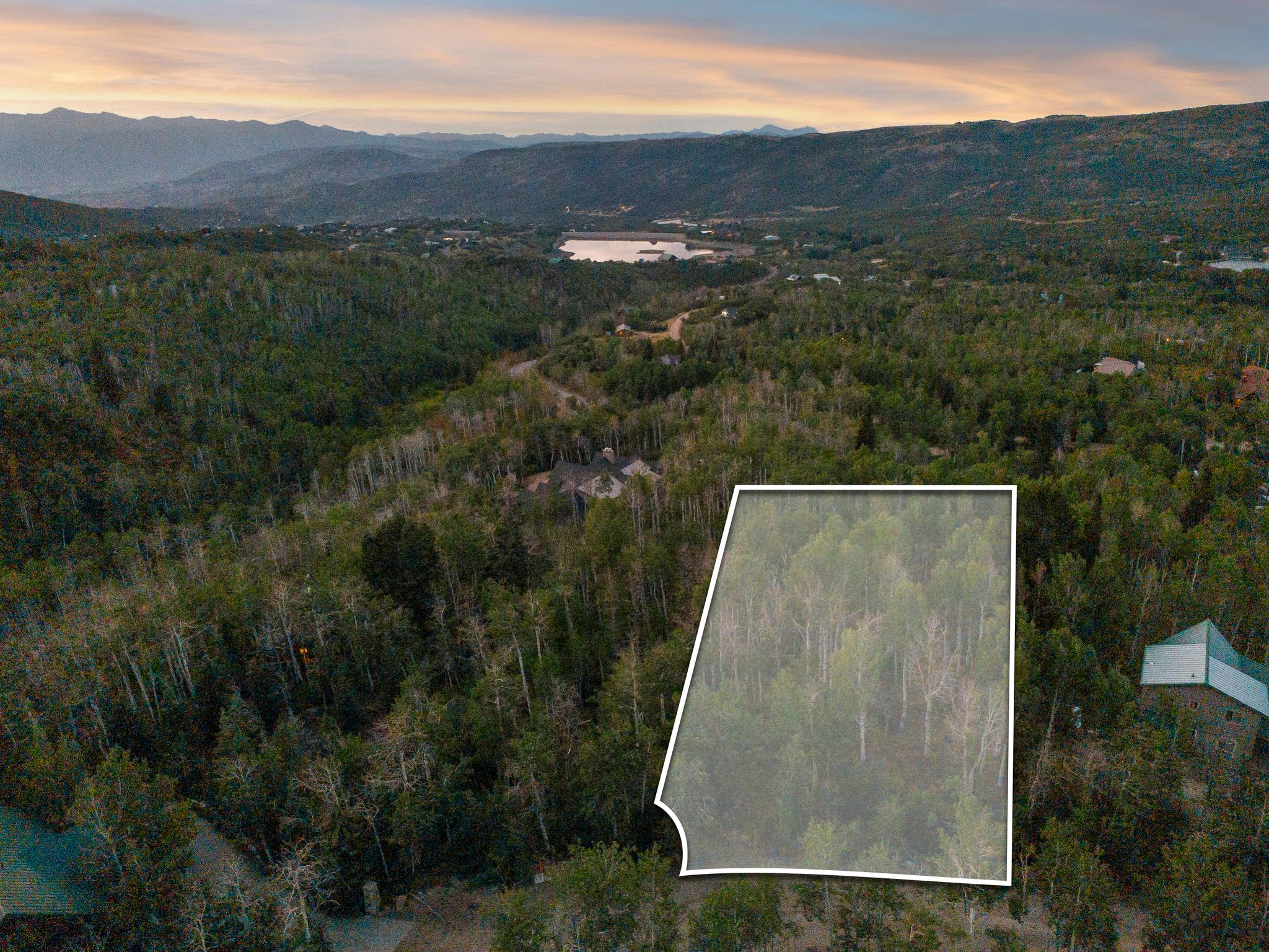 Aerial view at dusk of a water and mountain view, property parcel outlined, and a view of trees