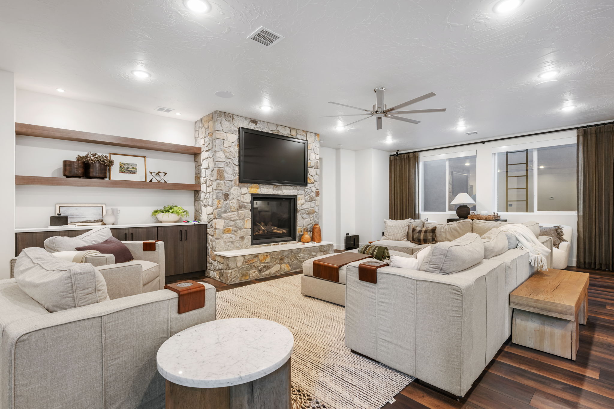Living room with a ceiling fan, wood finished floors, a stone fireplace, and recessed lighting