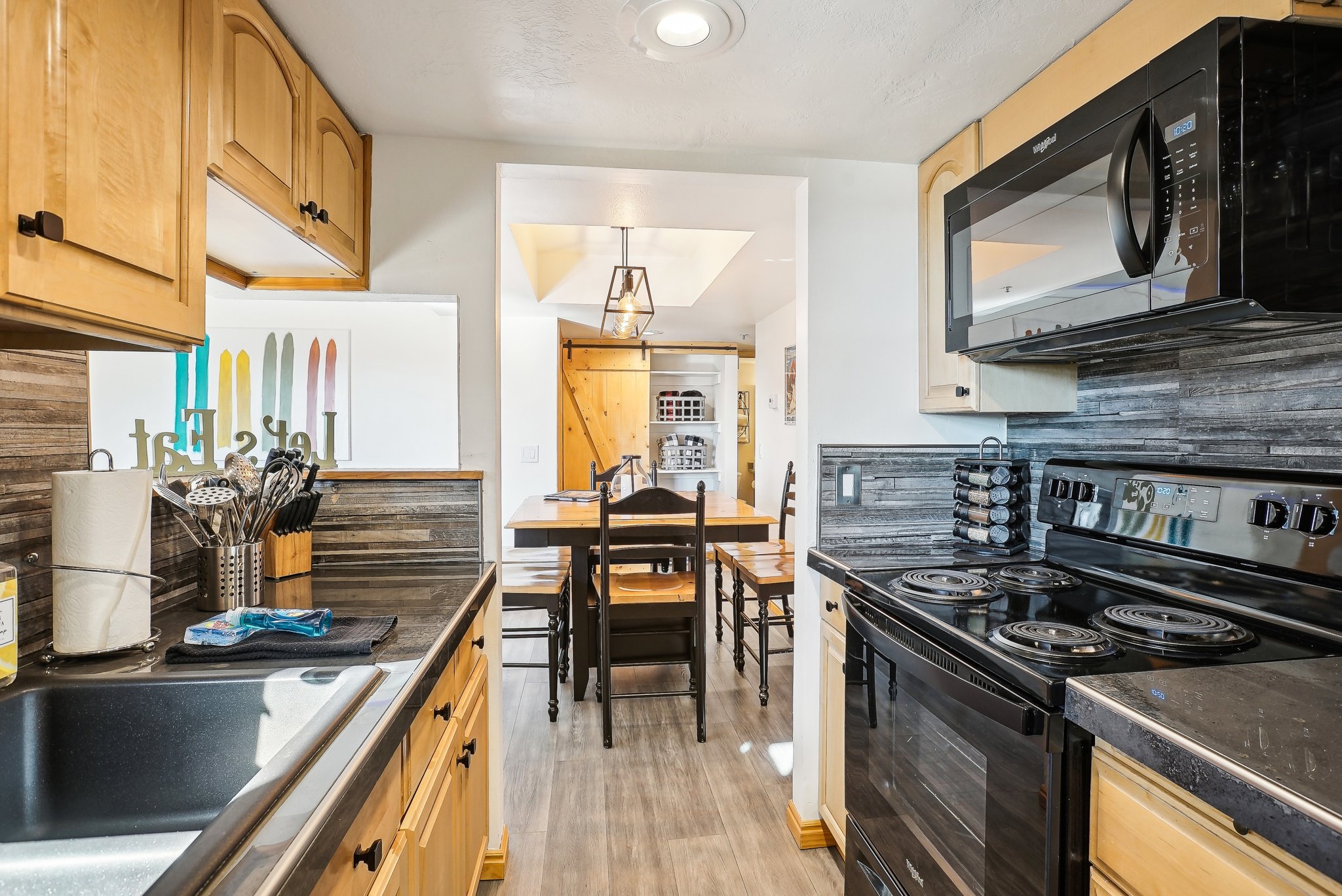 Kitchen with black appliances, dark countertops, light wood finish cabinets, decorative backsplash, and light wood finished floors