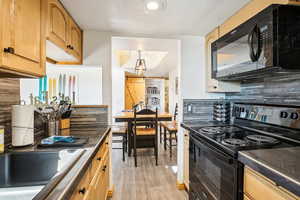 Kitchen with black appliances, dark countertops, light wood finish cabinets, decorative backsplash, and light wood finished floors