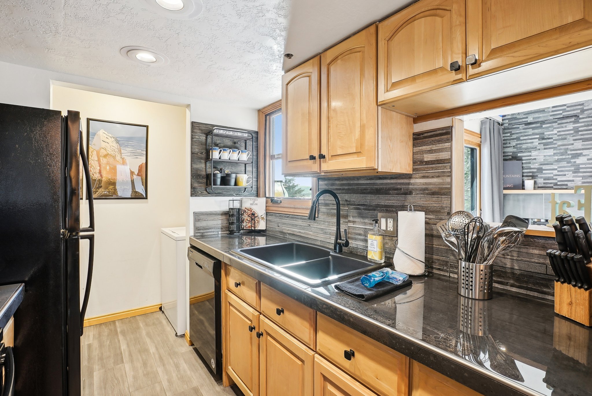 Kitchen with dark countertops, black appliances, light wood-style floors, backsplash, and a textured ceiling