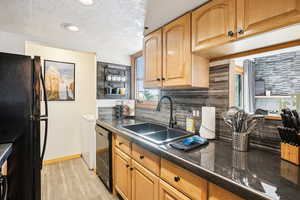 Kitchen with dark countertops, black appliances, light wood-style floors, backsplash, and a textured ceiling