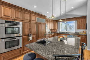 Kitchen with a breakfast bar area, double oven, an island with sink, and vaulted ceiling
