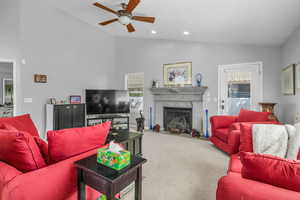 Carpeted living area with lofted ceiling, a fireplace with flush hearth, ceiling fan, healthy amount of natural light, and recessed lighting