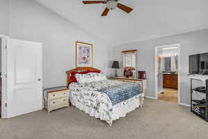 Primary bedroom featuring light carpet, ceiling fan, vaulted ceiling, and ensuite bathroom