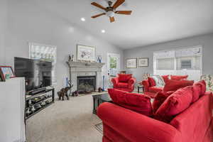 Carpeted living area featuring vaulted ceiling, a ceiling fan, a fireplace with flush hearth, and recessed lighting