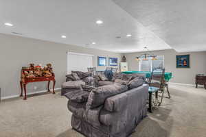 Basement living area featuring light colored carpet, a textured ceiling and recessed lighting