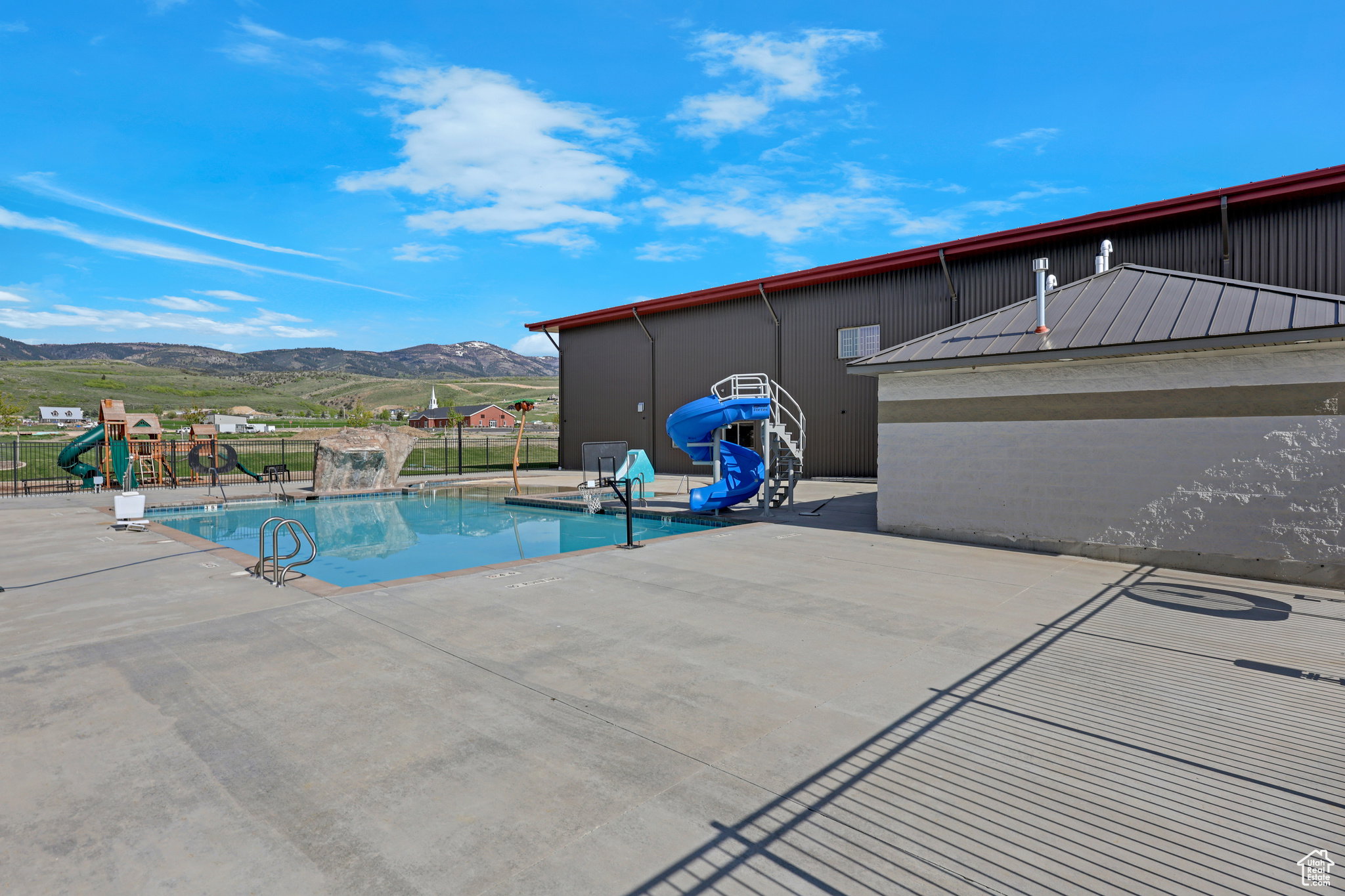 Community pool featuring a water slide, a mountain view, and a playground