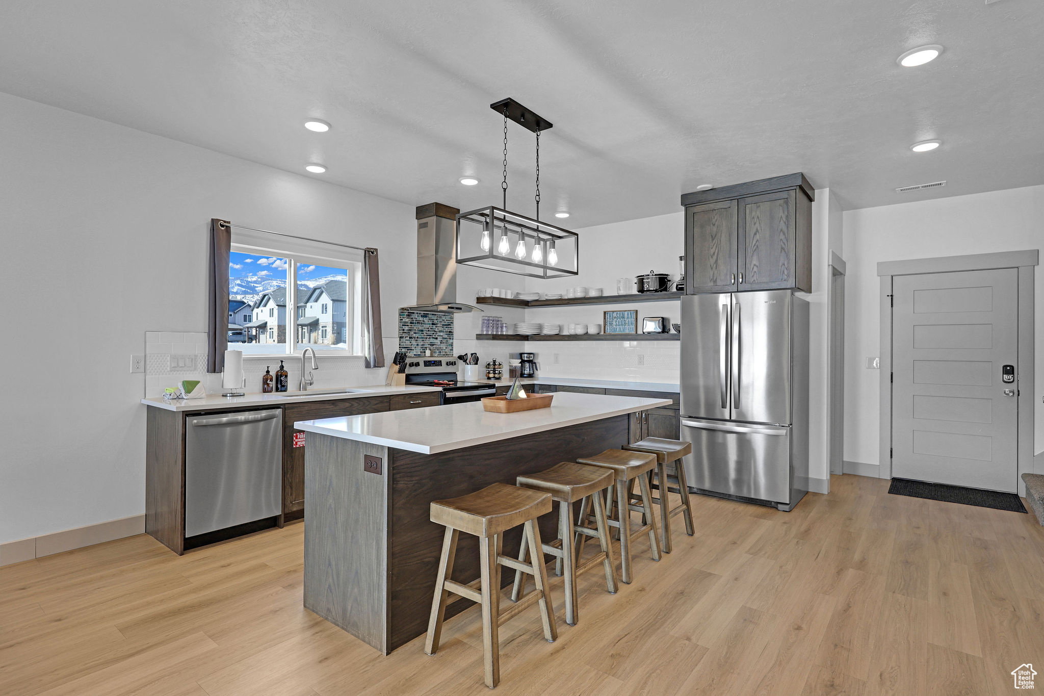 Kitchen with stainless steel appliances, decorative light fixtures, a kitchen island, and light wood-type flooring