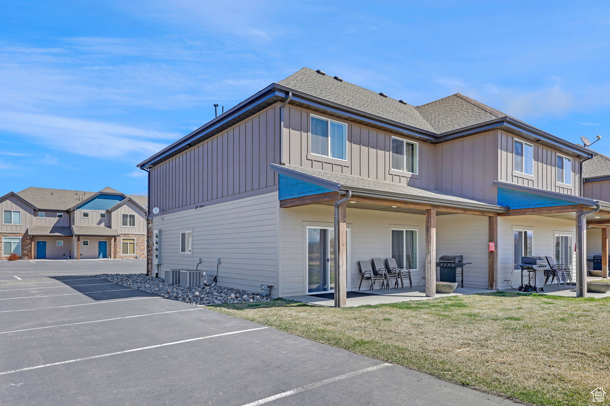 Back of property with uncovered parking, board and batten siding, a lawn, roof with shingles, and a residential view
