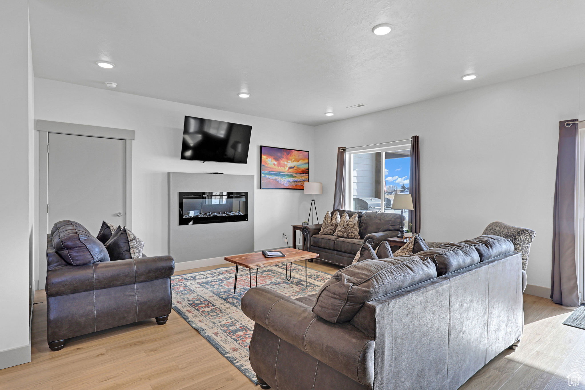 Living area with a glass covered fireplace, light wood finished floors, and recessed lighting