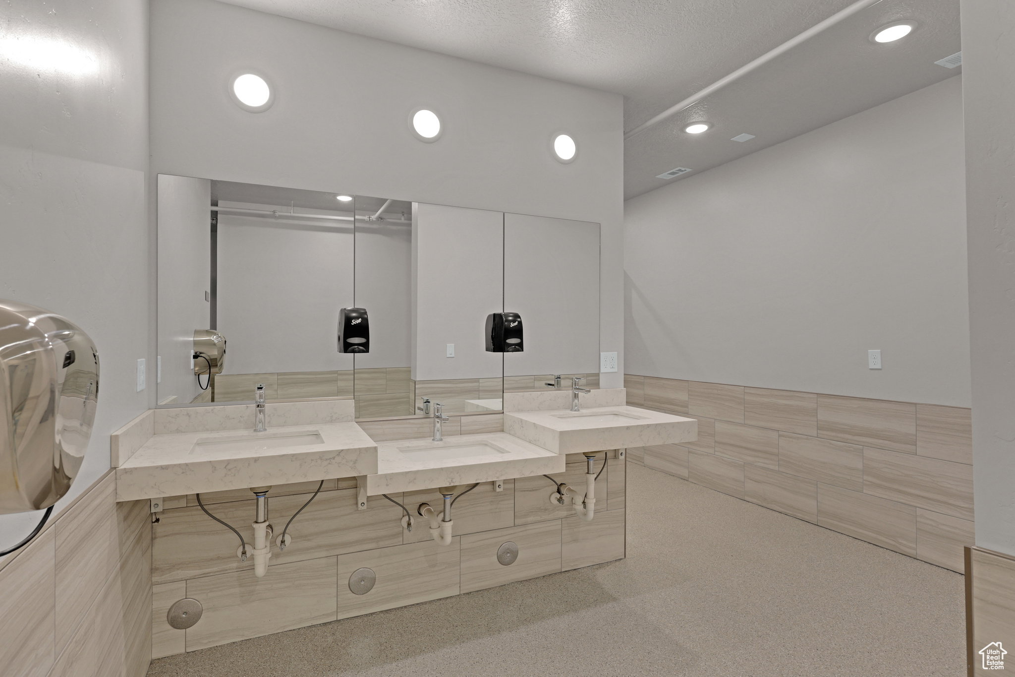 Bathroom with double vanity, tile walls, recessed lighting, and a wainscoted wall