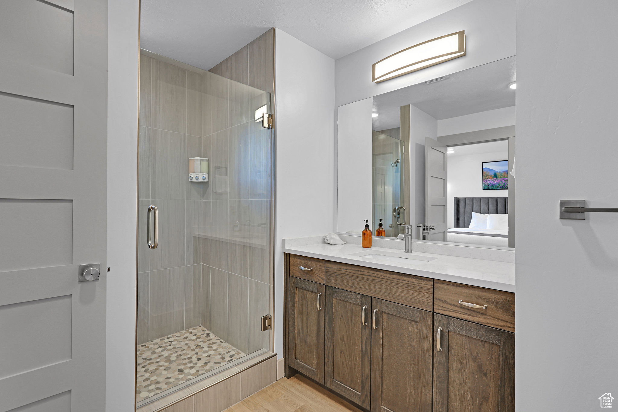 Ensuite bathroom featuring vanity, a shower stall, and light wood-style floors