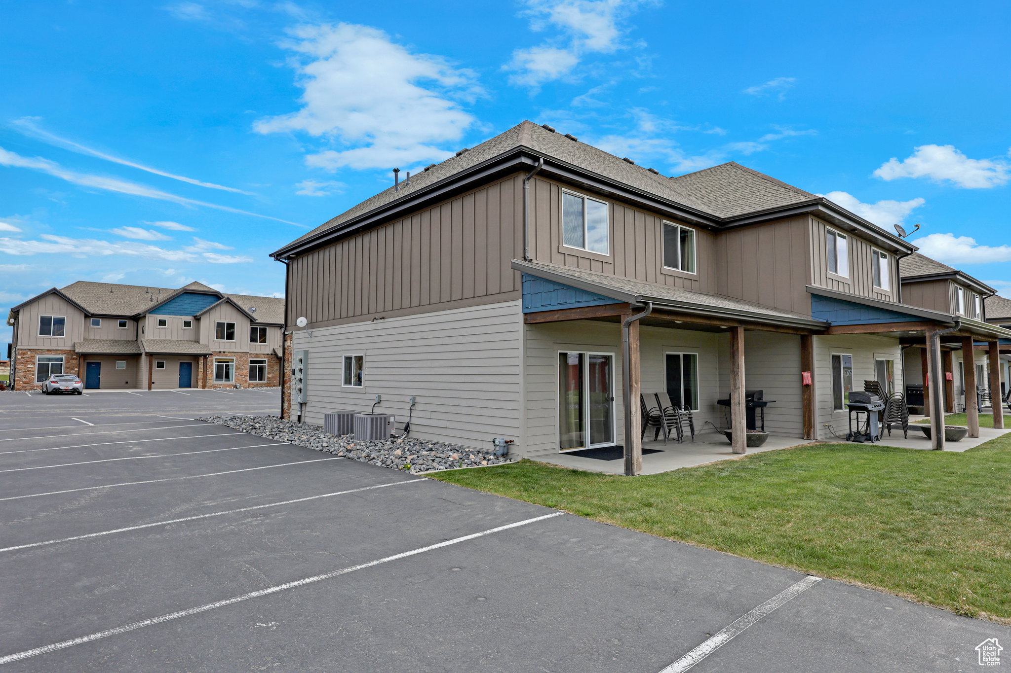 Rear view of house featuring uncovered parking, board and batten siding, a lawn, and a patio
