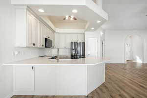 Kitchen featuring arched walkways, black appliances, a peninsula, recessed lighting, and light wood finished floors