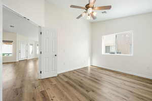 Empty room featuring ceiling fan, light wood-style floors, and a high ceiling