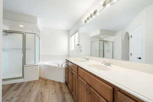 Full bath with a garden tub, double vanity, light wood finished floors, and a stall shower