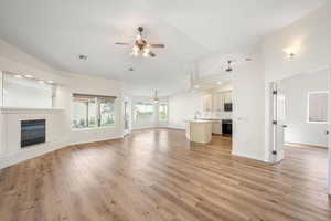 Unfurnished living room featuring a glass covered fireplace, a ceiling fan, light wood-style floors, and lofted ceiling