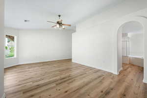 Spare room with arched walkways, ceiling fan, light wood-style flooring, and a textured ceiling