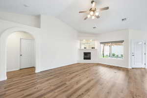 Unfurnished living room featuring a ceiling fan, arched walkways, a glass covered fireplace, light wood-type flooring, and vaulted ceiling