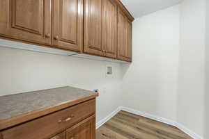 Laundry area with hookup for a washing machine, cabinet space, light wood-style flooring, a textured ceiling, and electric dryer hookup