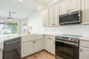 Kitchen with stainless steel appliances, vaulted ceiling, light wood-type flooring, light stone countertops, and decorative light fixtures