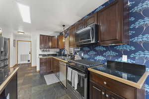 Kitchen with stainless steel appliances, stone finish floors, tile countertops, and dark wood finish cabinets