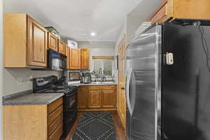 Kitchen featuring black appliances, wood finish cabinetry, recessed lighting, dark countertops, and dark wood-style floors