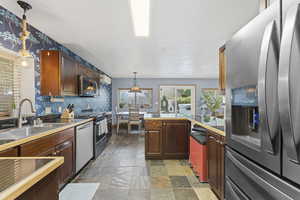 Kitchen with stainless steel appliances, stone finish floors, hanging light fixtures, a peninsula, and tile counters