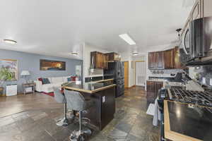 Kitchen with gas range, a breakfast bar area, black refrigerator with ice dispenser, stone tile flooring, and open floor plan