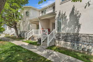 View of exterior entry with a porch, stucco siding, a yard, and stone siding