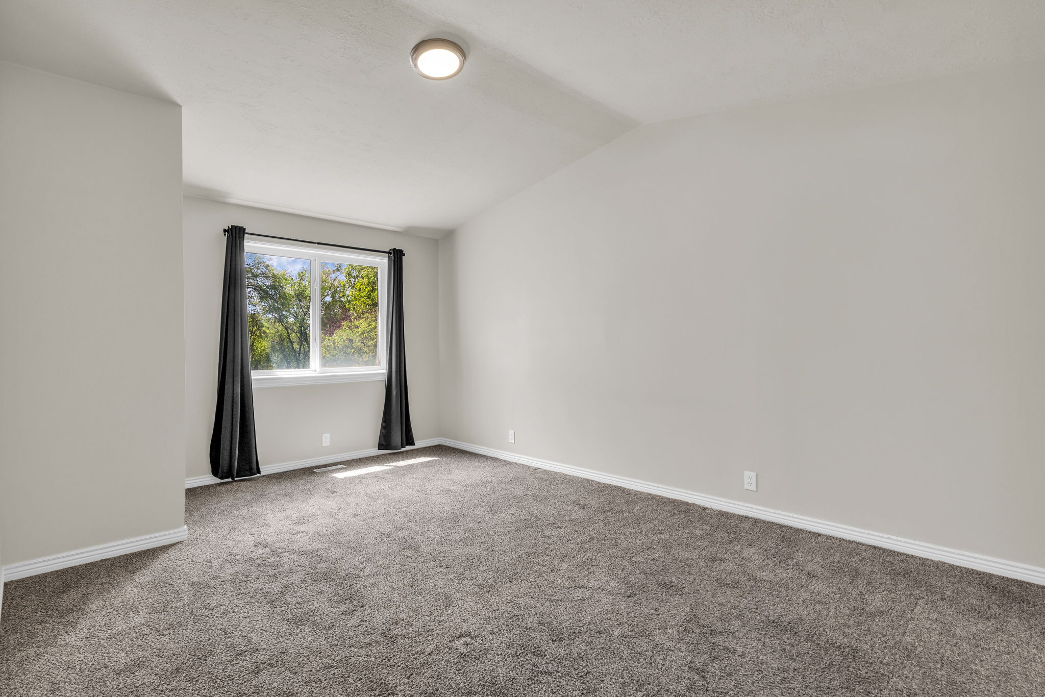 Carpeted spare room featuring baseboards and vaulted ceiling