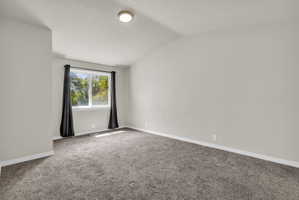Carpeted spare room featuring baseboards and vaulted ceiling
