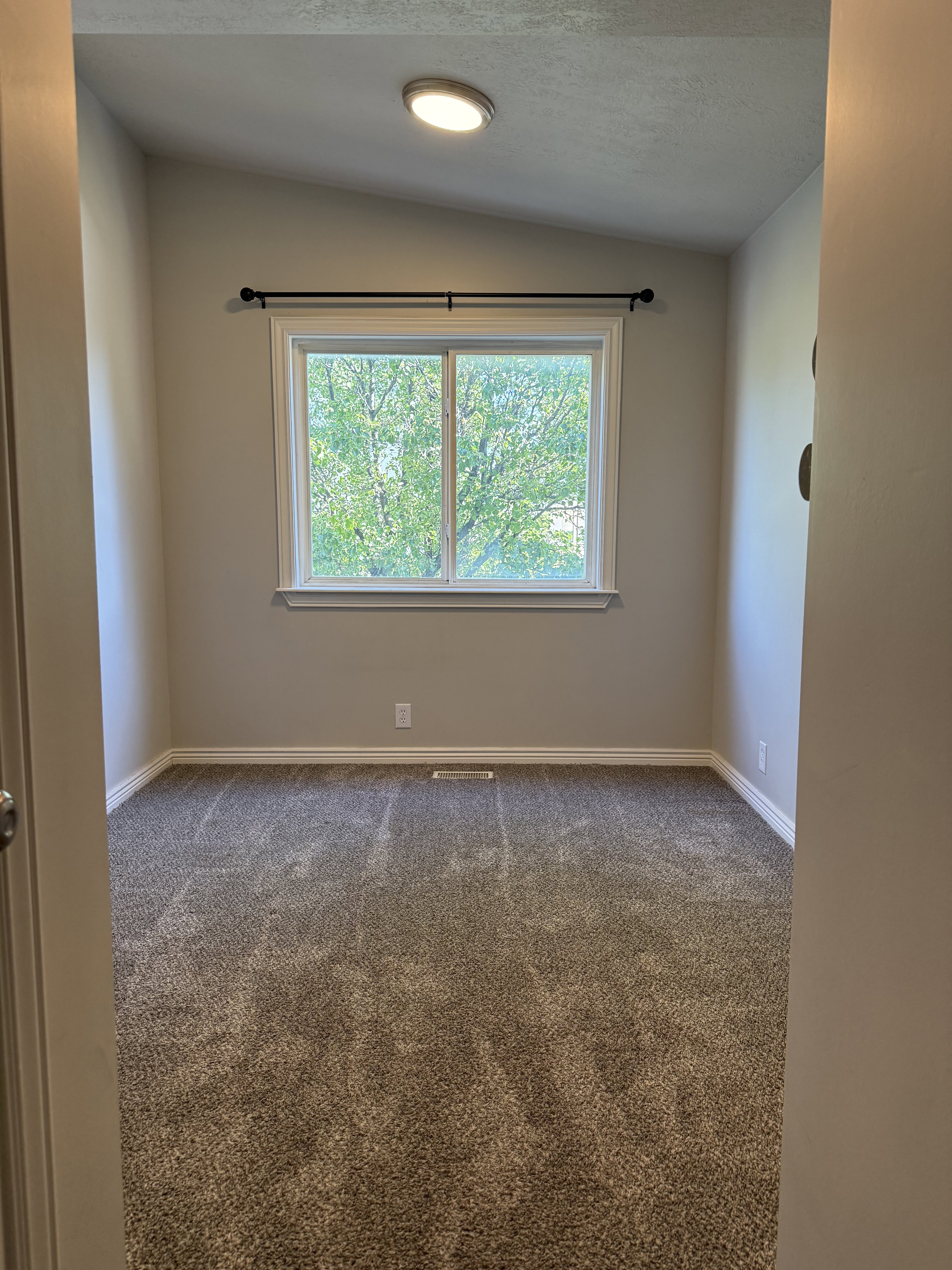 Room featuring a window with white trim, a black curtain rod, and a flush-mount ceiling light