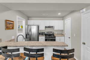 Kitchen with stainless steel appliances, a breakfast bar area, a peninsula, white cabinets, and recessed lighting