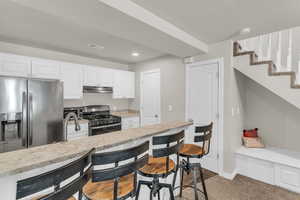 Kitchen with stainless steel appliances, white cabinetry, light stone countertops, a breakfast bar area, and recessed lighting