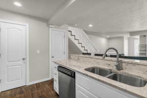 Kitchen with recessed lighting, white cabinets, light stone countertops, dark wood-style flooring, and stainless steel dishwasher