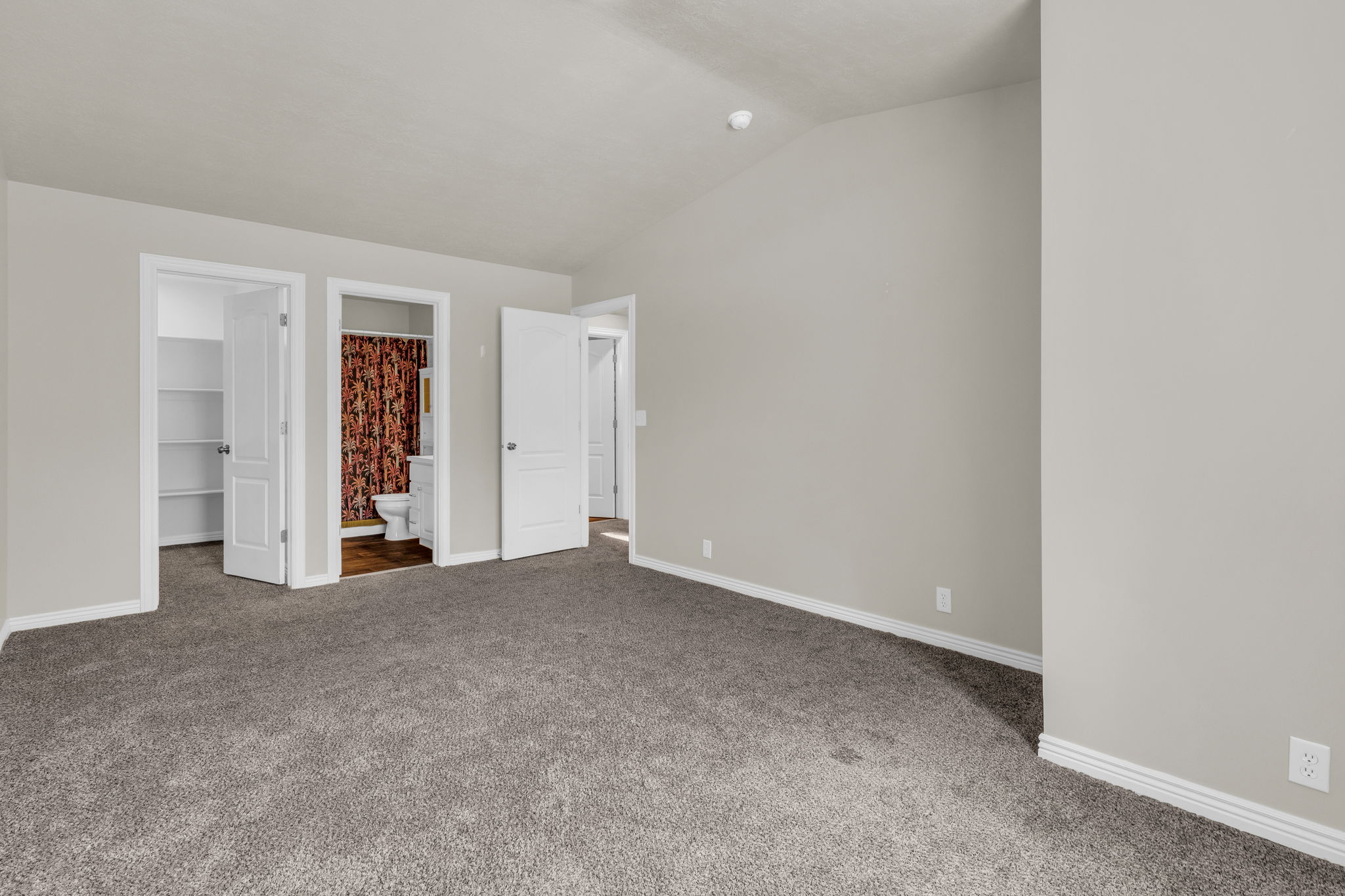 Unfurnished bedroom with a walk in closet, carpet floors, connected bathroom, and vaulted ceiling