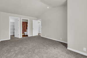 Unfurnished bedroom with a walk in closet, carpet floors, connected bathroom, and vaulted ceiling