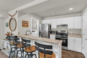 Kitchen with white cabinetry, stainless steel appliances, a breakfast bar, light stone countertops, and recessed lighting