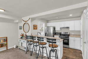 Kitchen featuring white cabinetry, a peninsula, stainless steel appliances, a breakfast bar area, and light stone countertops