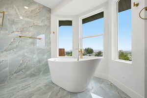 Full bathroom with light marble finish floors and a soaking tub
