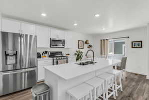 Kitchen featuring stainless steel appliances, a breakfast bar area, dark wood-type flooring, white cabinetry, and recessed lighting