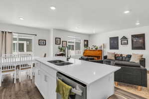 Kitchen with open floor plan, white cabinets, a center island with sink, dishwasher, and dark wood-style floors