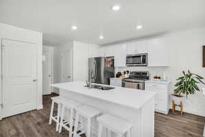 Kitchen featuring a kitchen bar, stainless steel appliances, a center island with sink, white cabinets, and dark wood finished floors